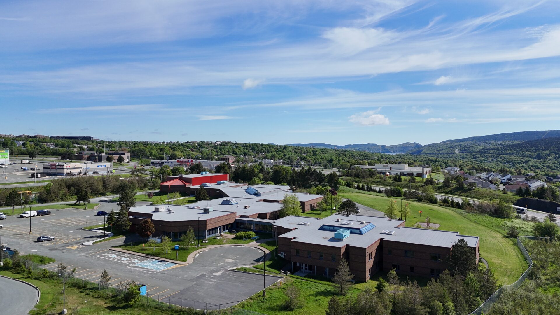 Aerial view of a large building with red and gray roofs next to a highway