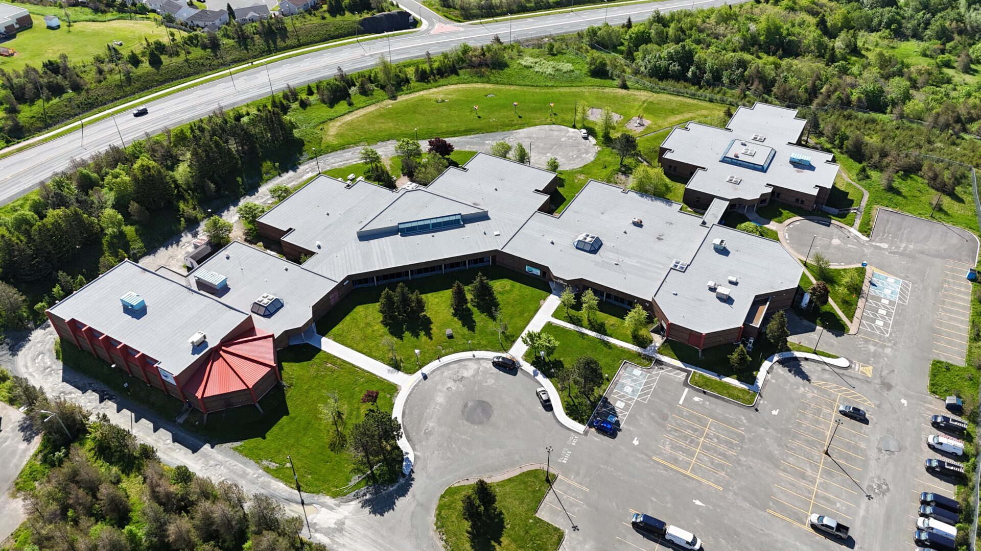 Aerial view of a large building with red and gray roofs next to a highway