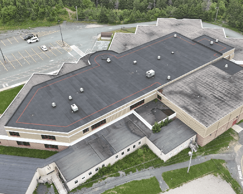 Aerial view of a large single-story building with a dark roof and surrounding parking lot